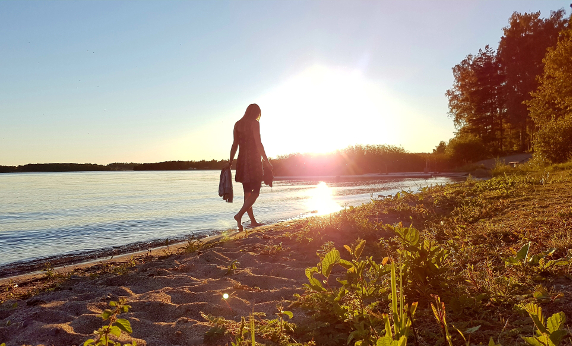 Kvinna vandrande längs strand i solnedgång