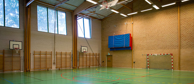 Sportthall med grönt golv, ribbstolar och basketkorgar