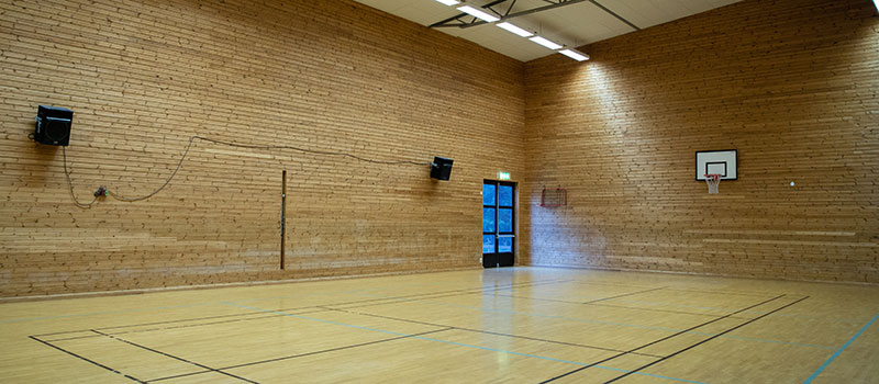 Sporthall med trägolv, träväggar och basketkorg.